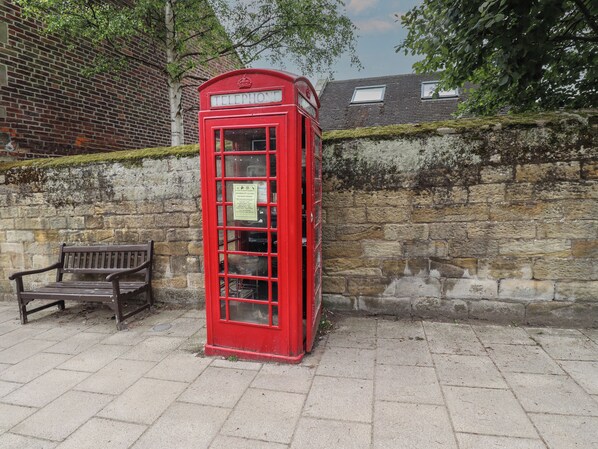 A red telephone booth with a bench nearby. - Lark Rise (Alnwick)