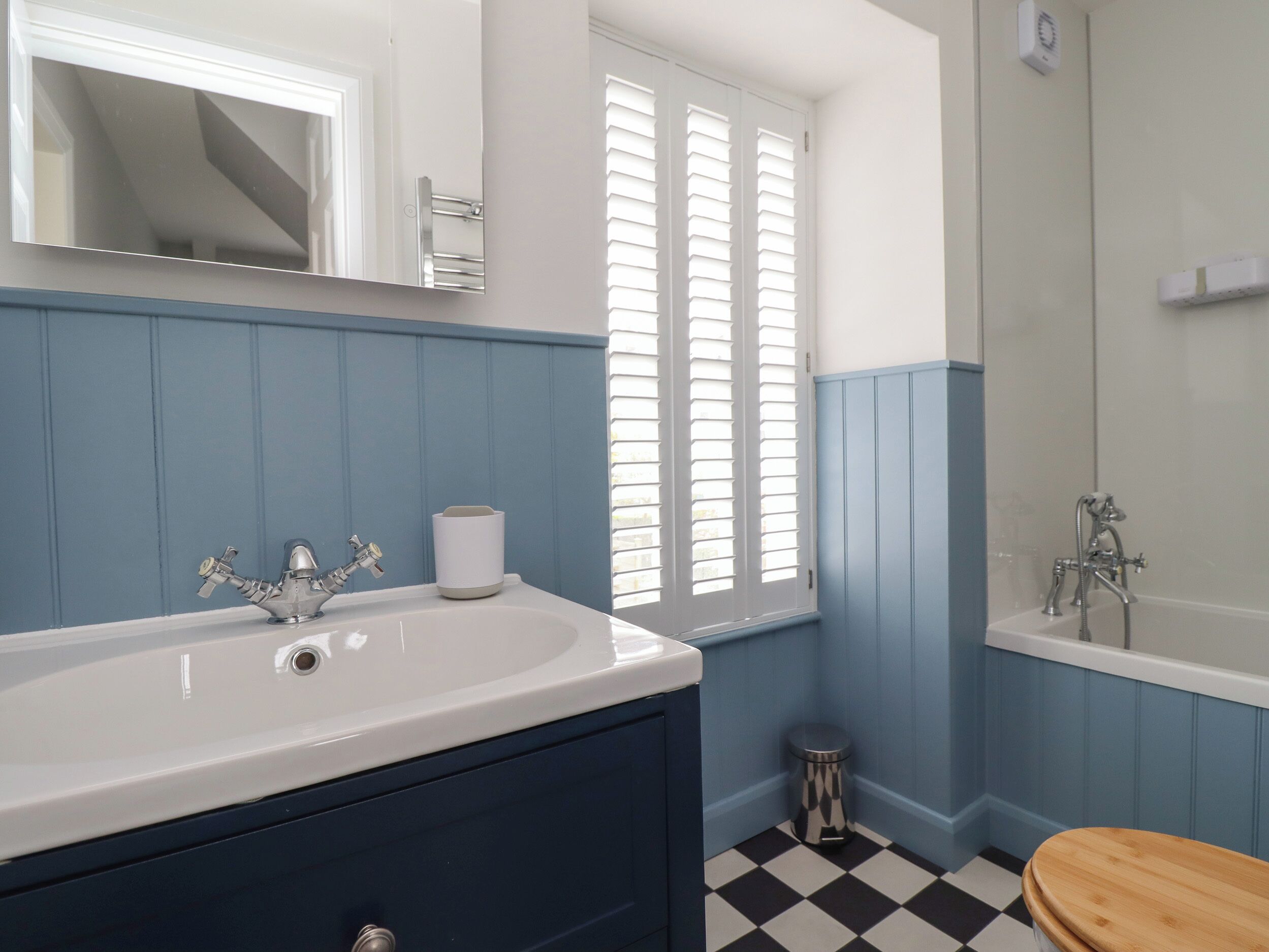 A bathroom with a white sink, blue walls, a wooden toilet, and a black and white checkered floor.