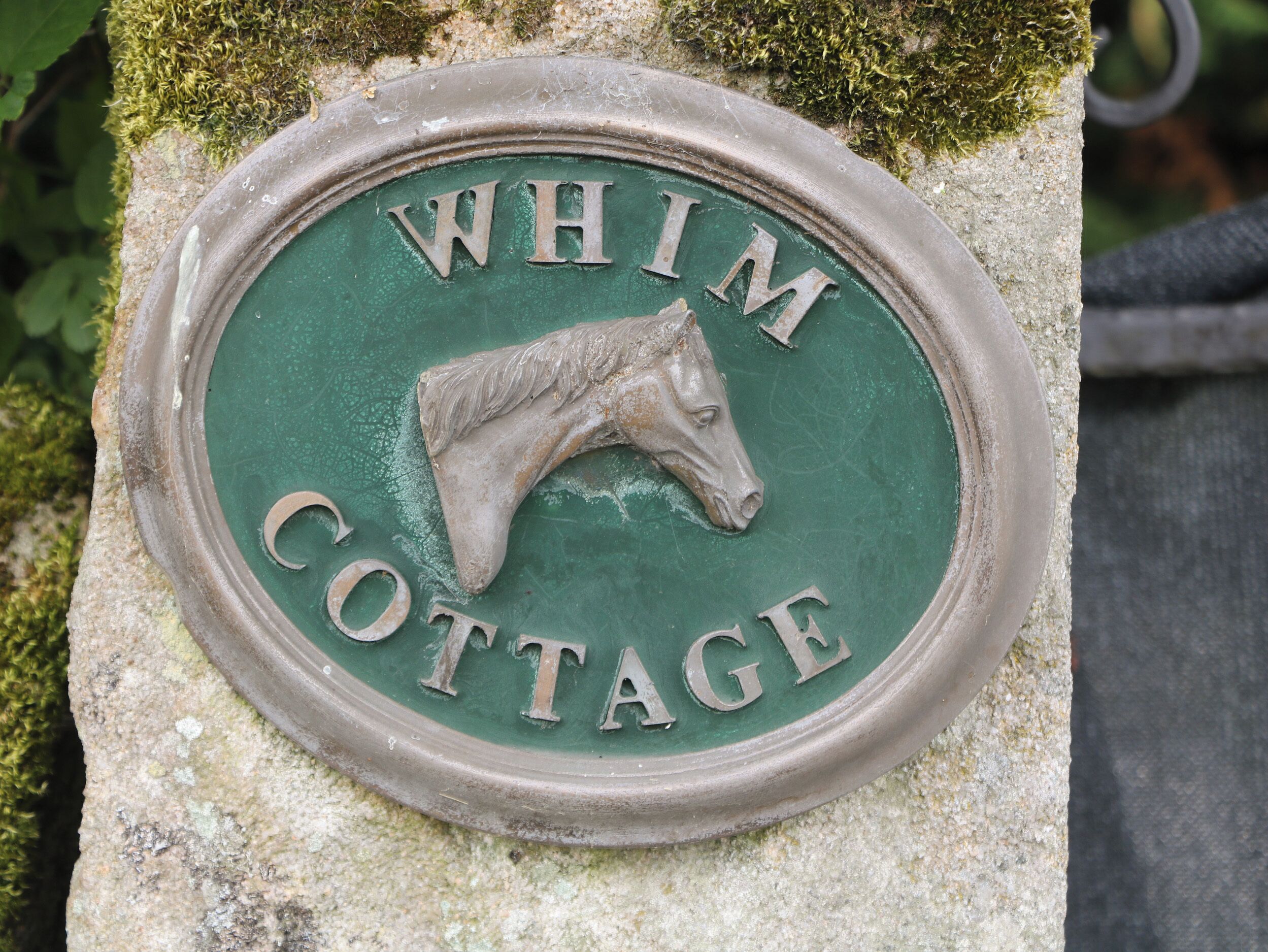 A metal plaque with the inscription "WHIM COTTAGE" and a horse head emblem.