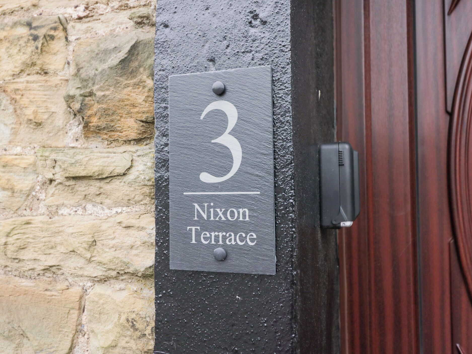A house number sign with the number 3 and the name "Nixon Terrace" on a black wall.