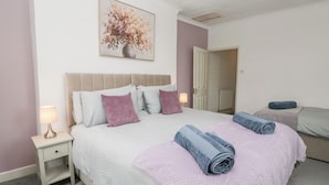 A bedroom with a bed, nightstands, a painting, and a door leading to another room. - 3 Nixon Terrace (Maryport)