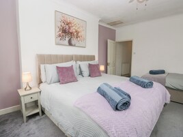 A bedroom with a bed, nightstands, a painting, and a door leading to another room.