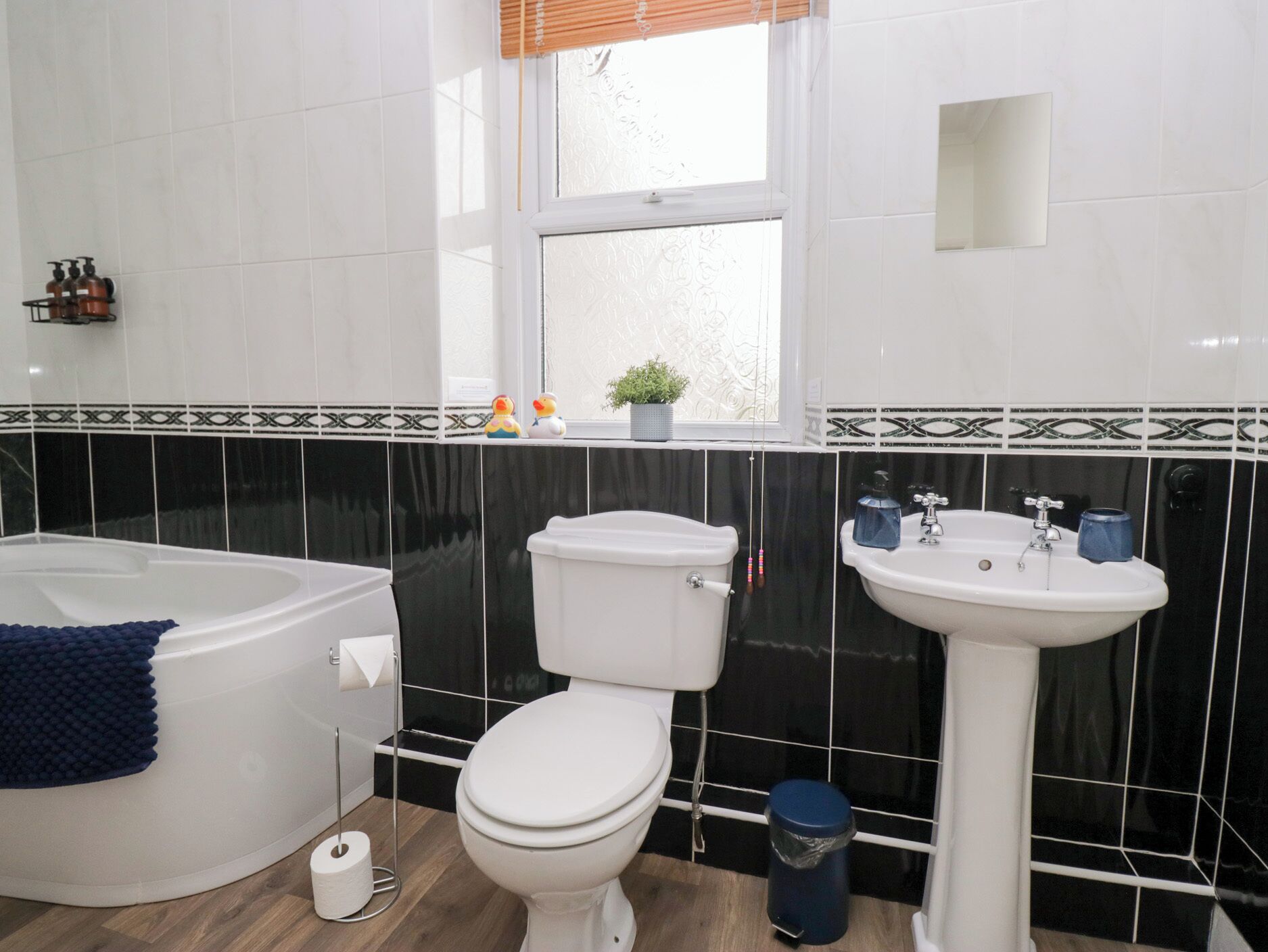Un bagno con vasca, water e lavabo, caratterizzato da piastrelle bianche e nere e una finestra.
