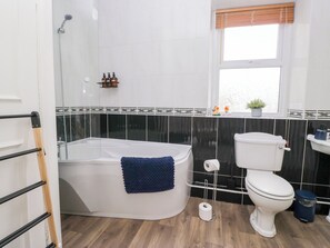 A bathroom with a bathtub, toilet, and a window. - 3 Nixon Terrace (Maryport)