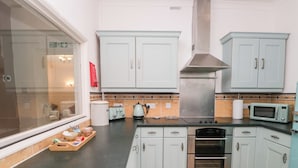 A kitchen with white cabinets, a stainless steel range hood, a microwave, a toaster, and a wooden countertop. - 3 Nixon Terrace (Maryport)