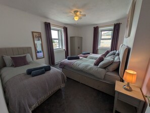 A bedroom with two beds, a ceiling fan, and a bedside lamp. - 3 Nixon Terrace (Maryport)