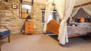 A bedroom with a stone wall, a wooden bed with a canopy, a nightstand, a dresser, and a mirror. - Up Over Head (Penzance)