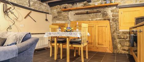 A cozy kitchen with a dining table, wooden chairs, and a stone wall.