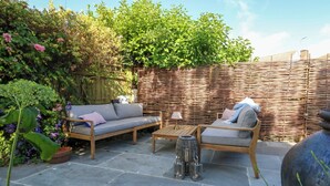 Un patio con sofá, sillón y mesa de centro, rodeado de piso de piedra y cerca de madera.