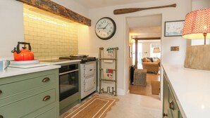 Una cocina con armarios verdes, un hervidor, un reloj y una viga de madera sobre el fregadero.