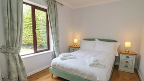 Un lit bien fait, avec du linge de lit blanc et des oreillers, deux lampes de chevet, un plancher en bois et une fenêtre avec des rideaux.
