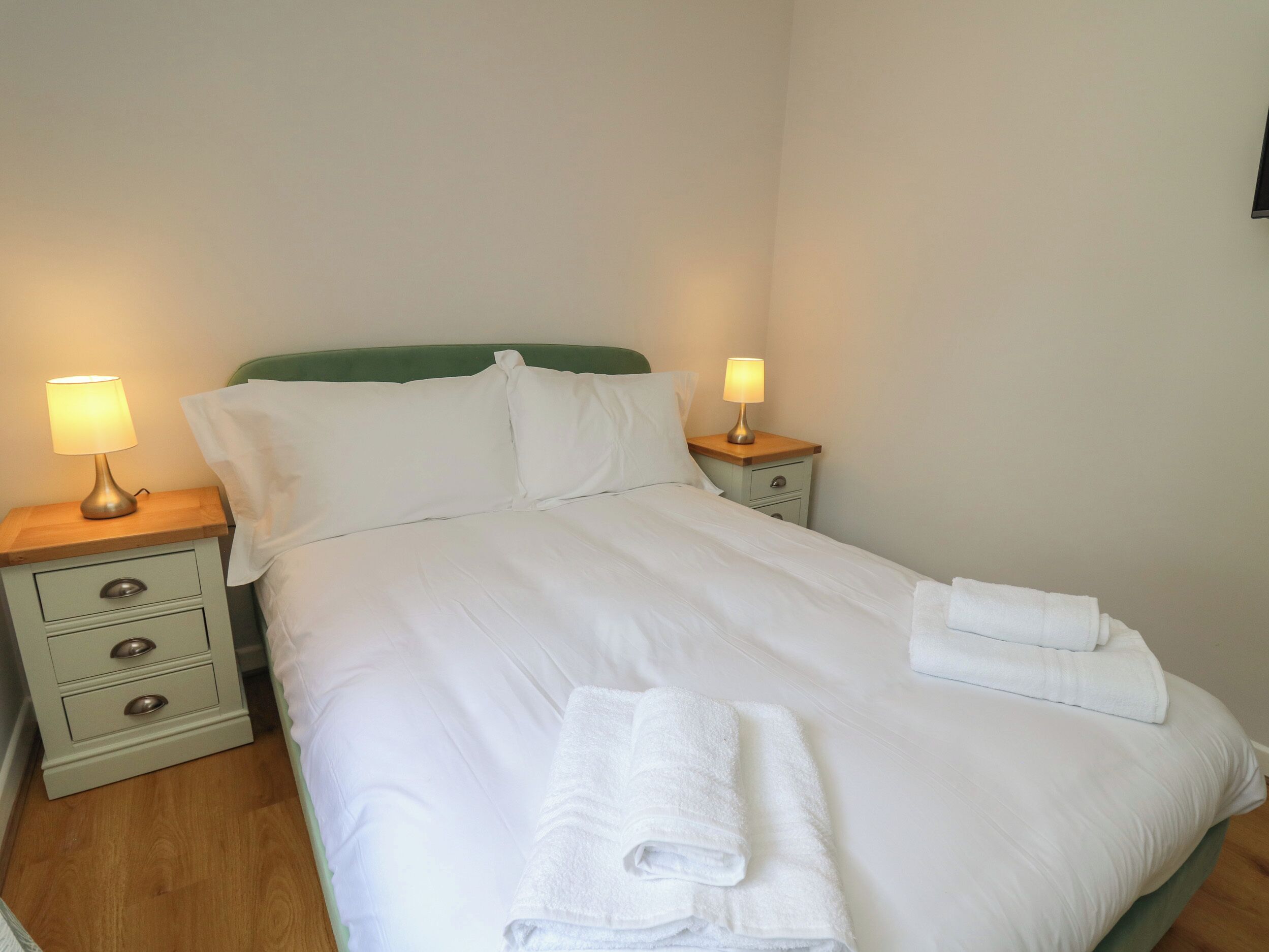 A neatly made bed with white linens, two bedside lamps, and a green headboard.
