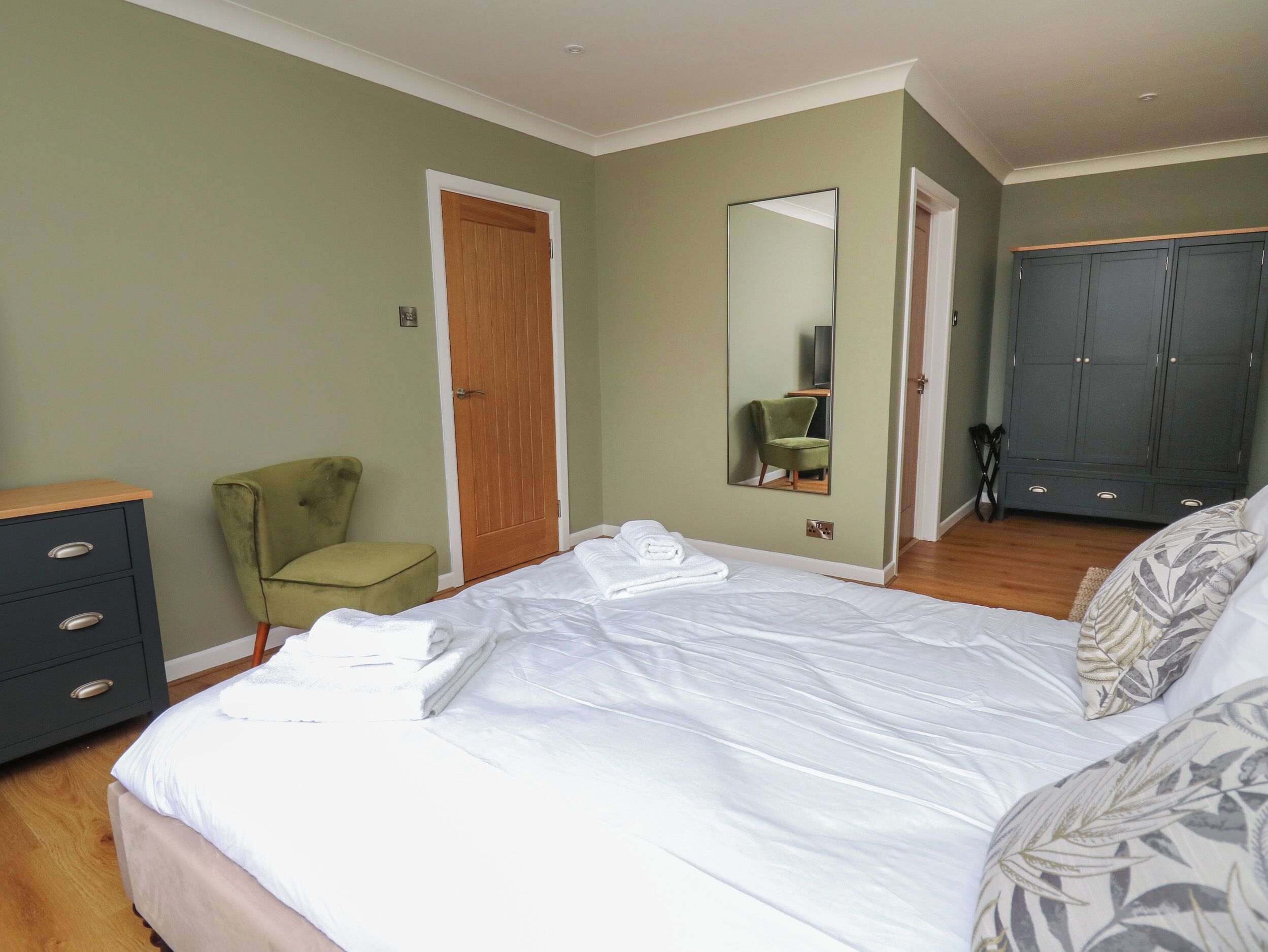 Een slaapkamer met een bed, een groene fauteuil, een kledingkast en een spiegel.