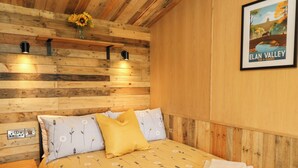 Une pièce aux murs lambrissés, comprenant un lit, une table de chevet, une lampe fixée au mur et un tableau encadré.