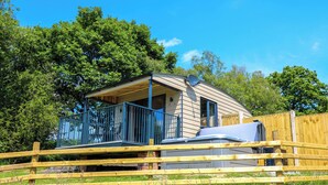 Une petite cabane à un seul étage, dotée d’un balcon, entourée d’une clôture en bois et d’une végétation luxuriante.