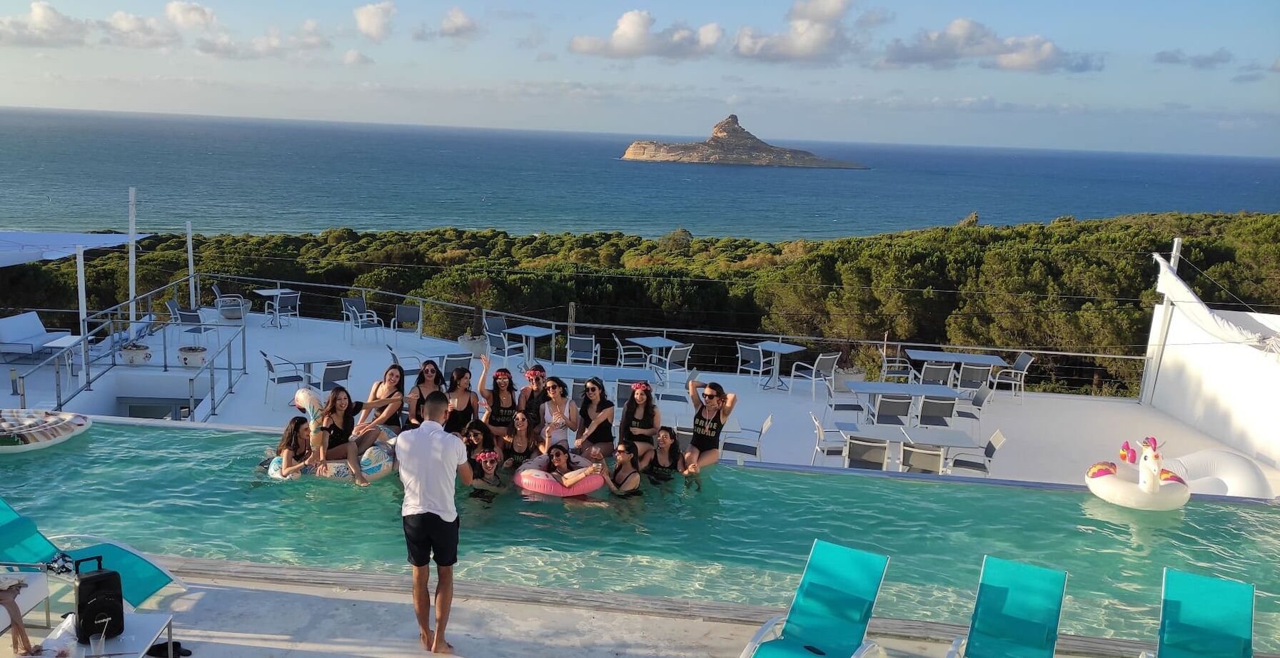 A group of people in a pool with a view of the sea and an island in the distance.