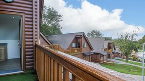 Een houten chalet met een balkon, een deur die naar een kamer leidt en een uitzicht op andere chalets op de achtergrond.