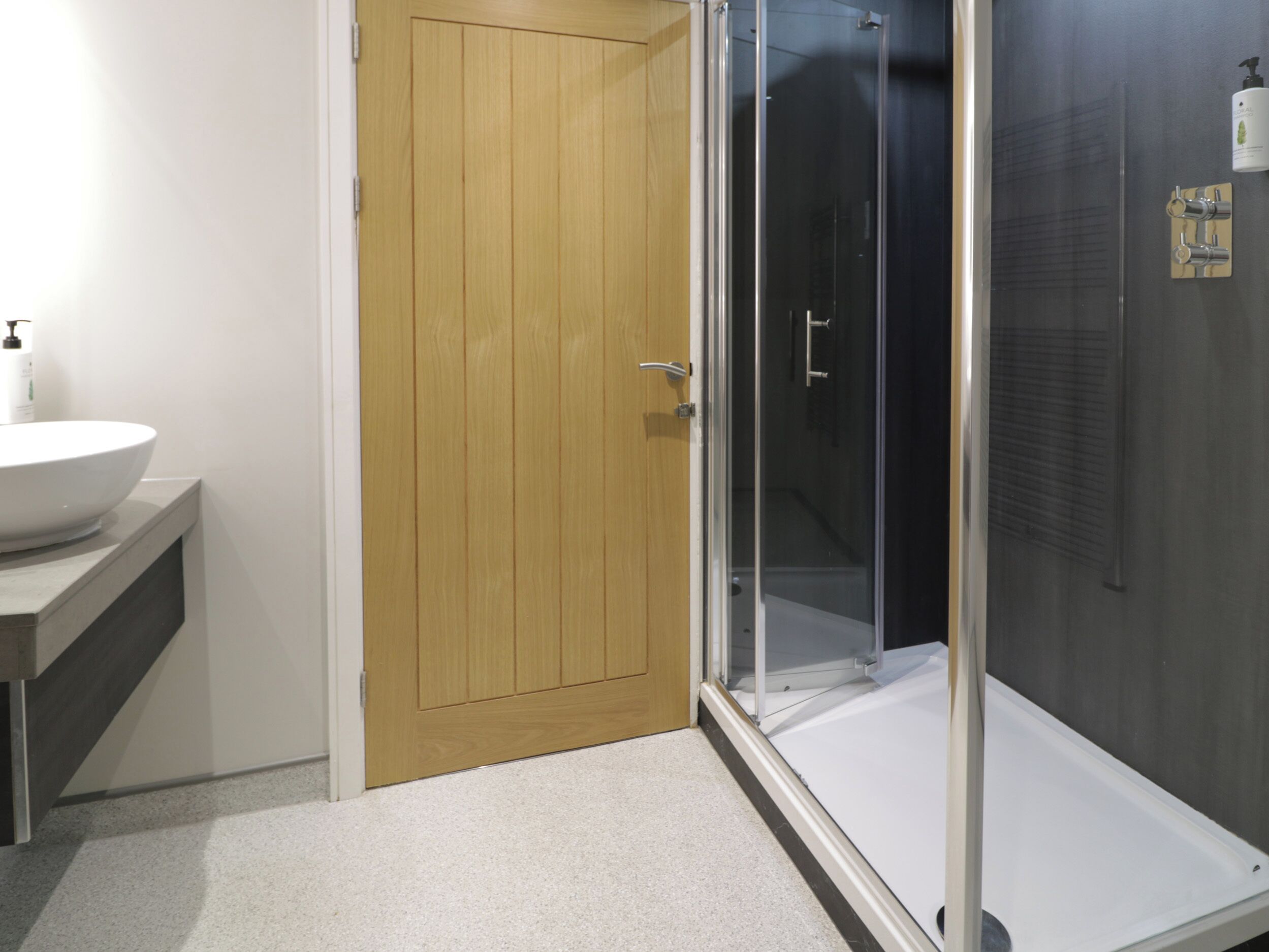 A bathroom with a wooden door, a white sink, and a glass-enclosed shower.