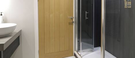 A bathroom with a wooden door, a white sink, and a glass-enclosed shower.