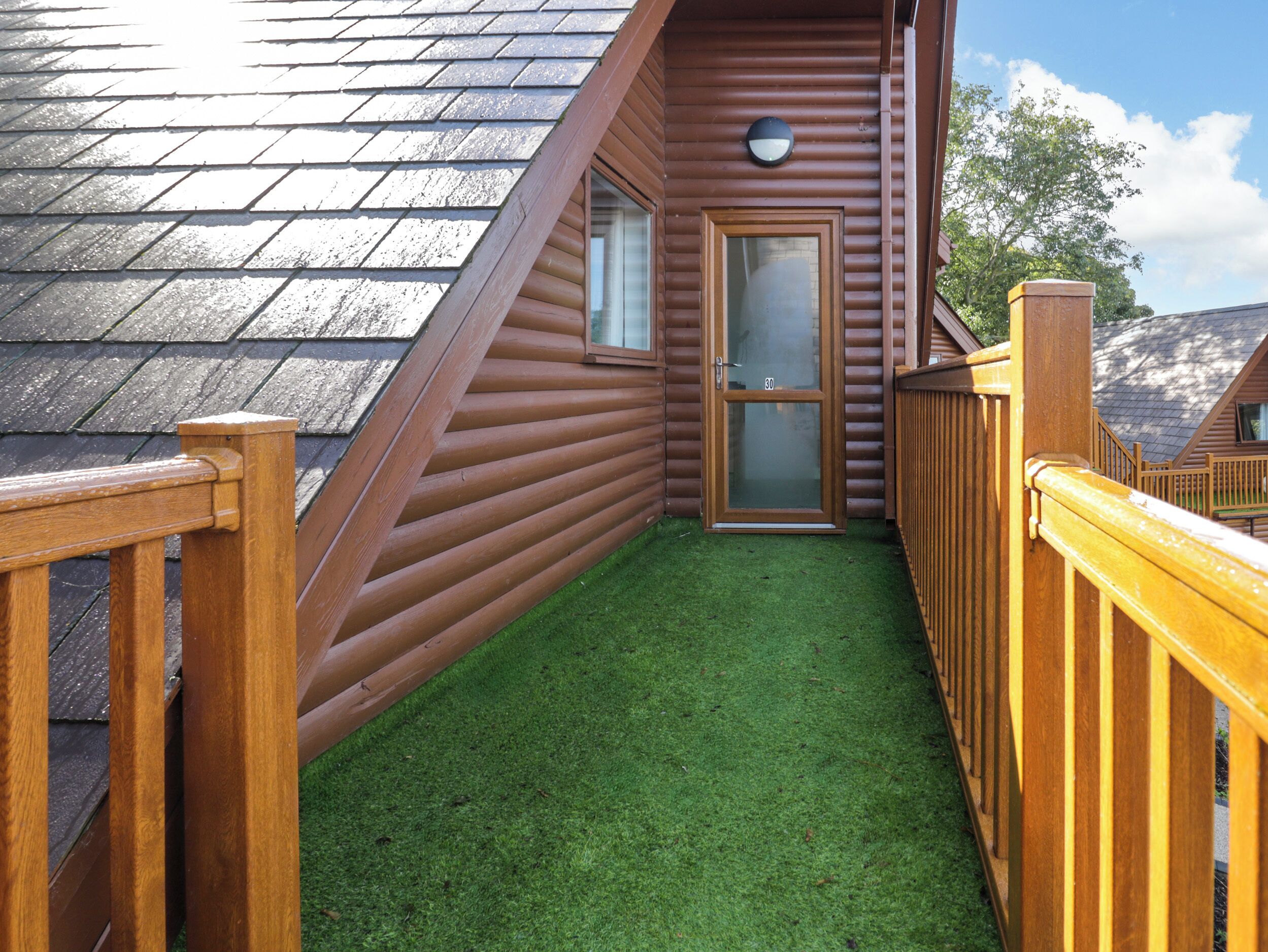 A wooden deck with a glass door leading to a small enclosed area with artificial grass.