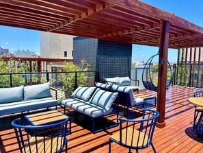 A rooftop terrace with a wooden deck, blue and white striped sofa, and a hanging chair. - Hyde Park Comfort 1 (Joao Pessoa)