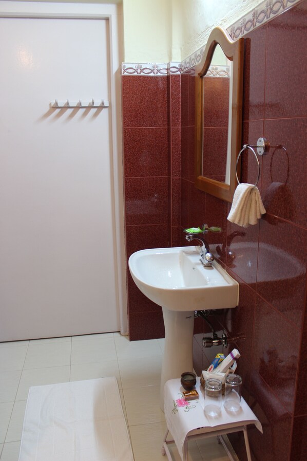 Une salle de bain avec un lavabo blanc, un porte-serviettes, un miroir et une petite table sur laquelle sont posés des articles de toilette.