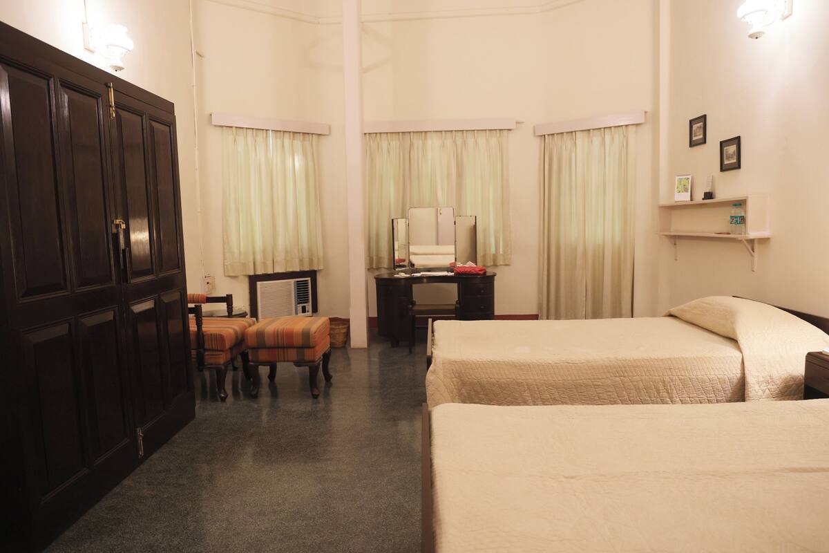 Ein Hotelzimmer mit zwei Betten, einem Schreibtisch mit Stuhl, einem Kleiderschrank und einem kleinen Tisch mit Spiegel.
