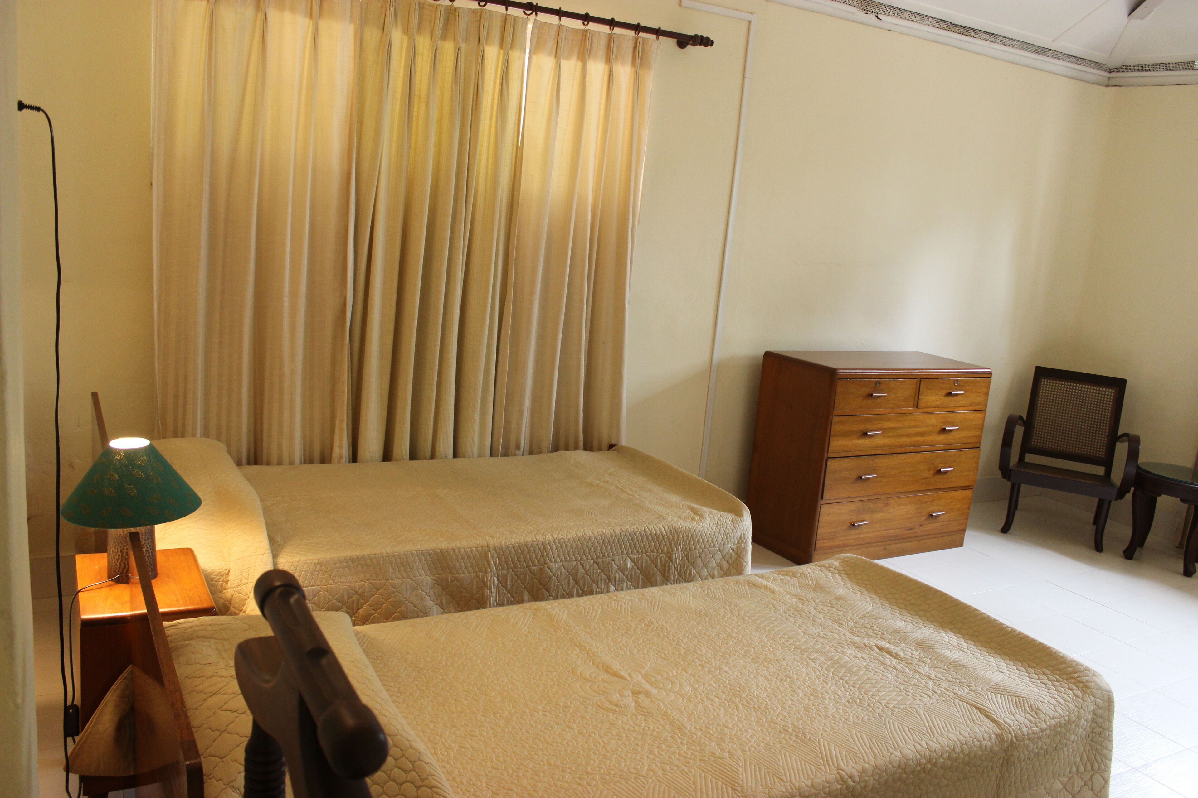 A bedroom with two beds, a wooden dresser, a chair, and a lamp.