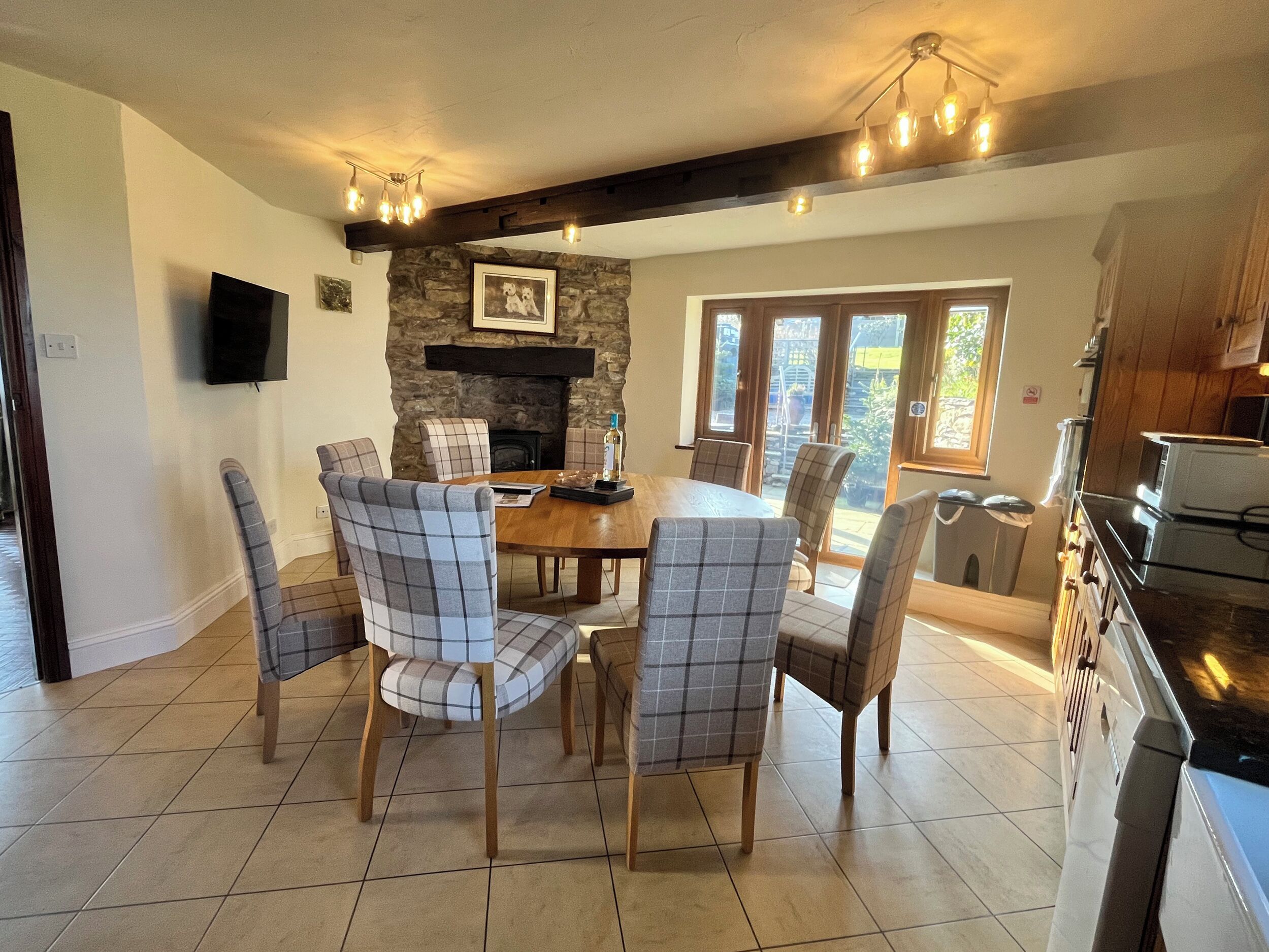 A dining area with a stone fireplace, a wooden table, and six plaid chairs.