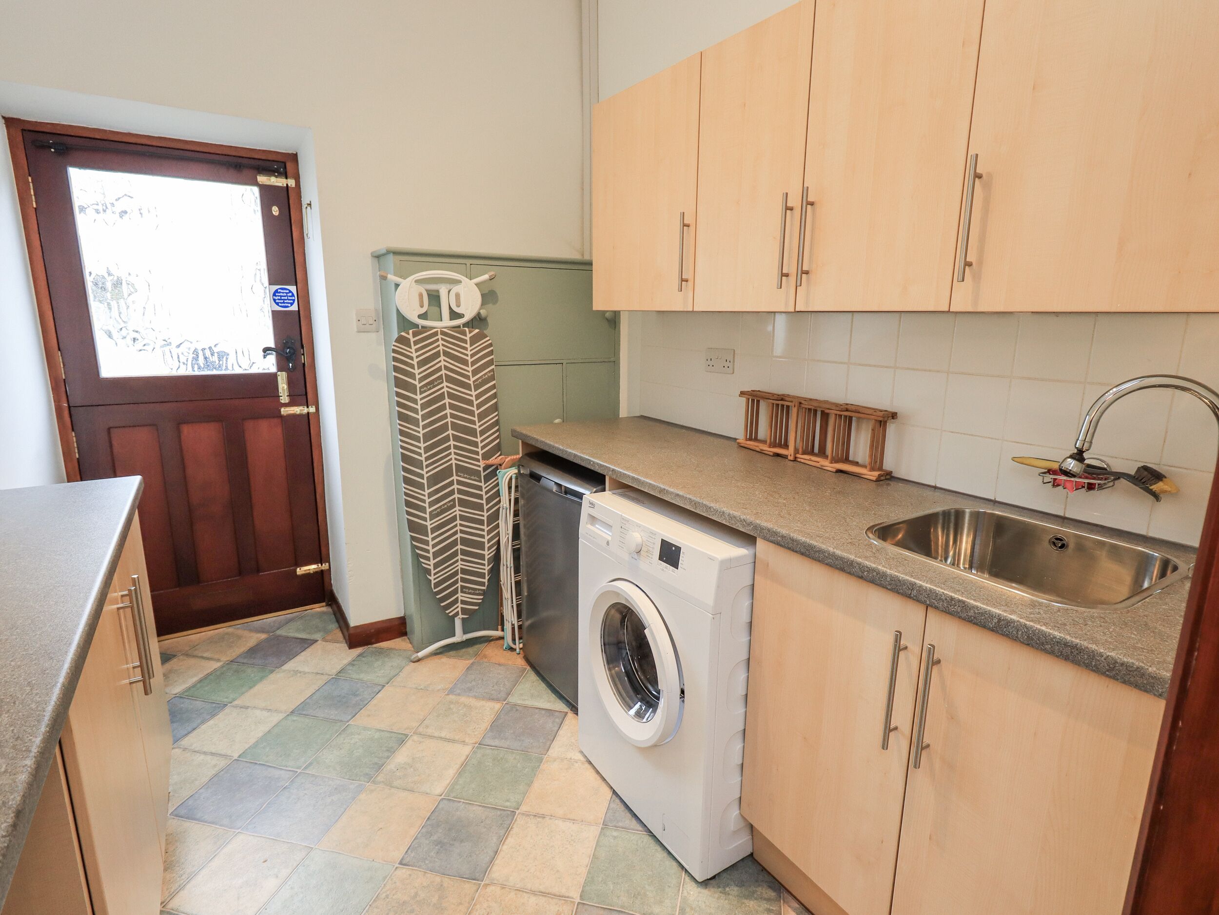 A compact kitchen with a washing machine, a sink, and wooden cabinets.