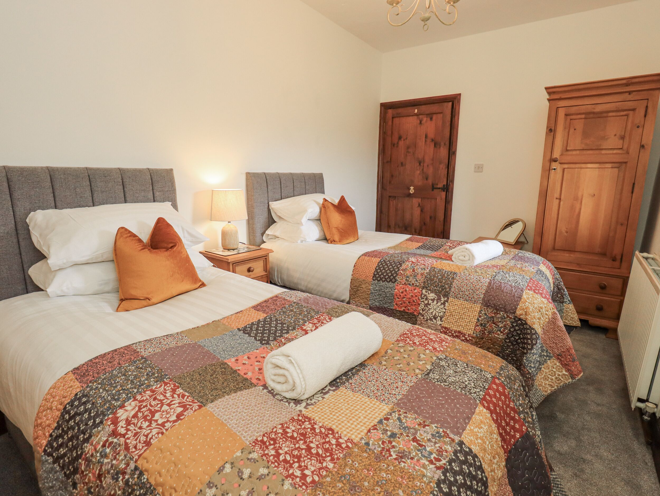 A hotel room with two beds, each with a quilted bedspread and pillows. There is a nightstand with a lamp between the beds.