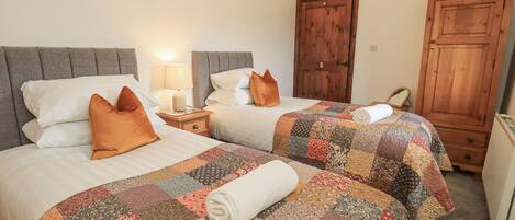 A hotel room with two beds, each with a quilted bedspread and pillows. There is a nightstand with a lamp between the beds.
