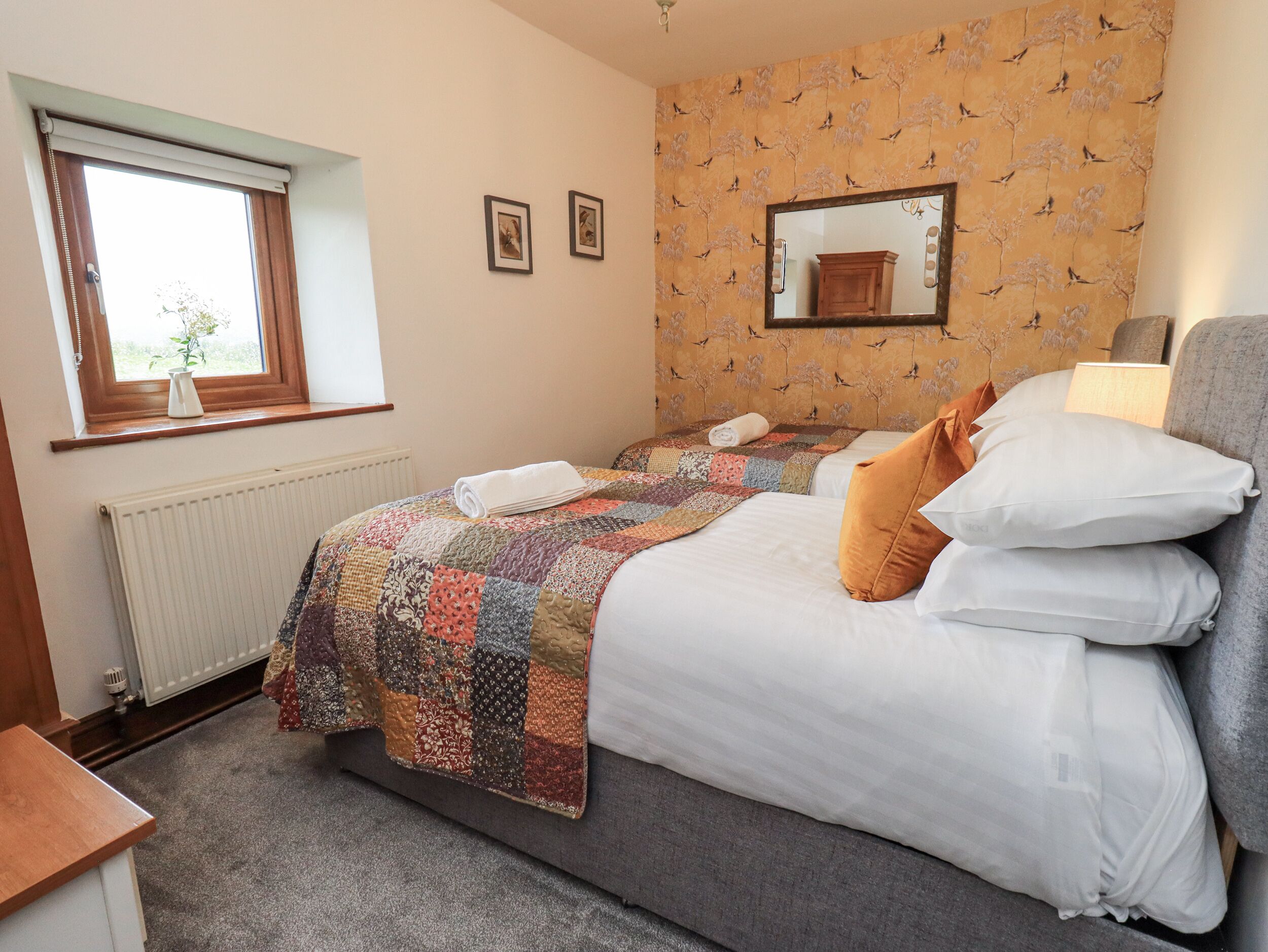 A bedroom with a large bed, a window with a view, a radiator, and a patterned wallpaper.