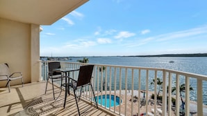 A balcony with two chairs and a table, overlooking a swimming pool and the sea.