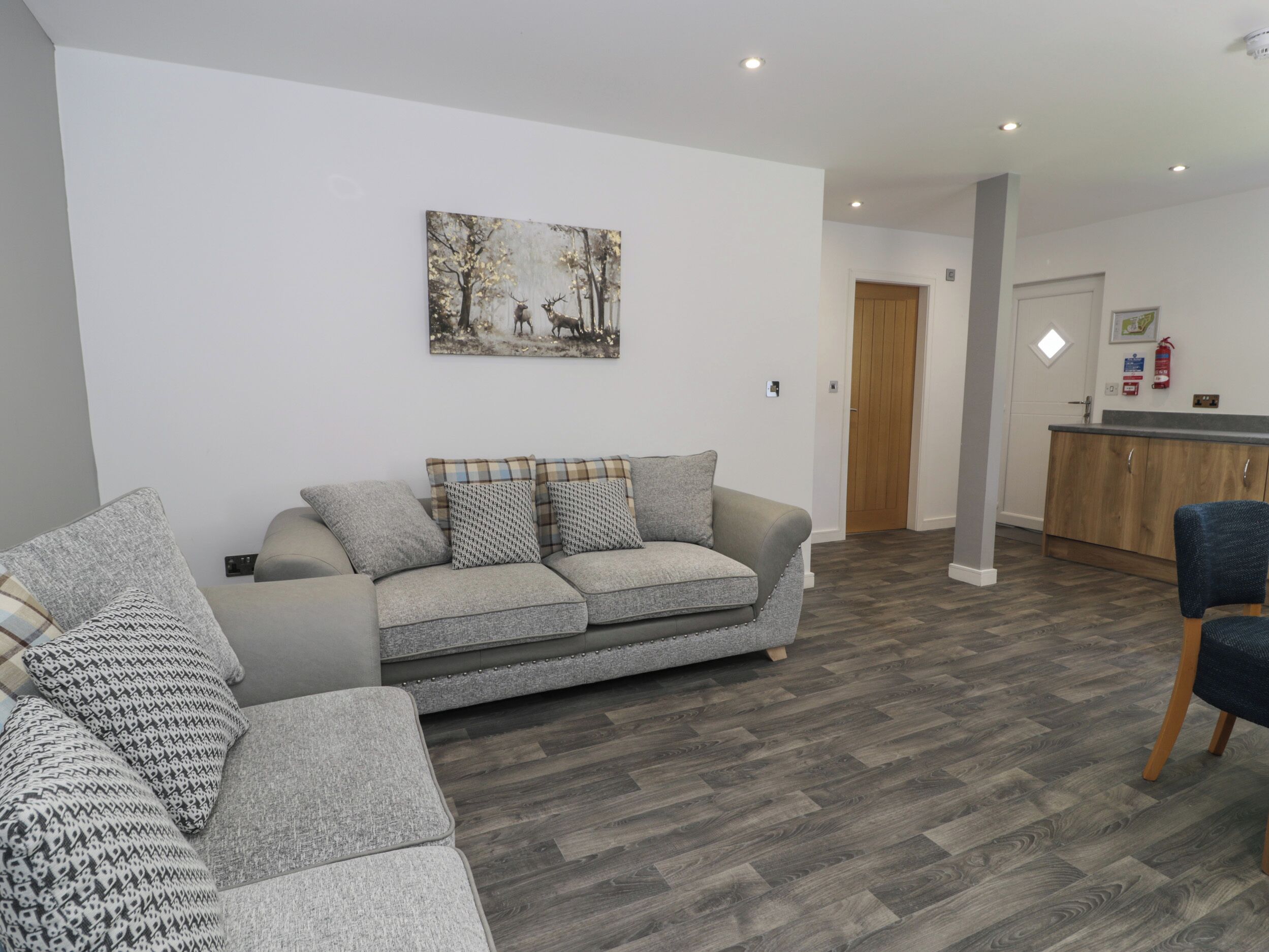 A modern living room with a grey sofa, patterned cushions, and a painting of deer on the wall.