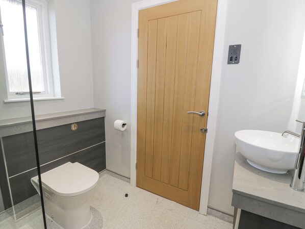A bathroom with a toilet, a wooden door, a sink, and a window. - Classic Lodge 16 (Rhyl)