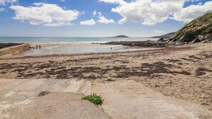 A beach with rocky terrain, a concrete walkway, and distant hills. - Shells Cottage (Looe)