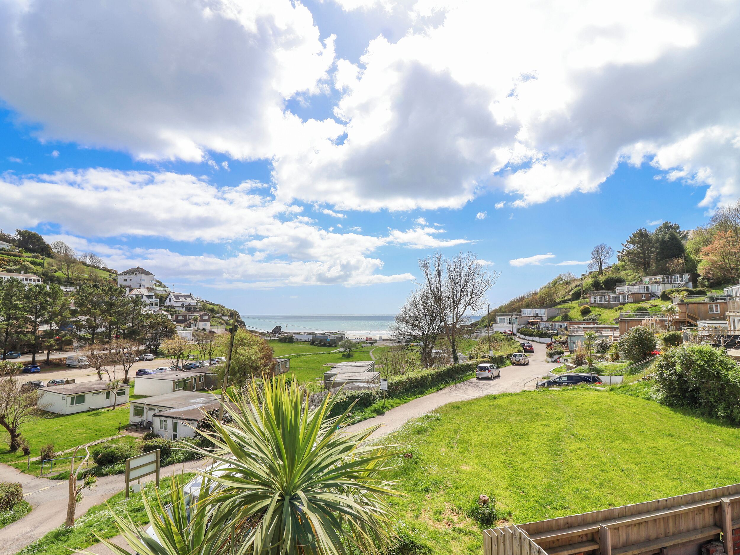 A coastal residential area with houses, a grassy field, and a view of the sea.