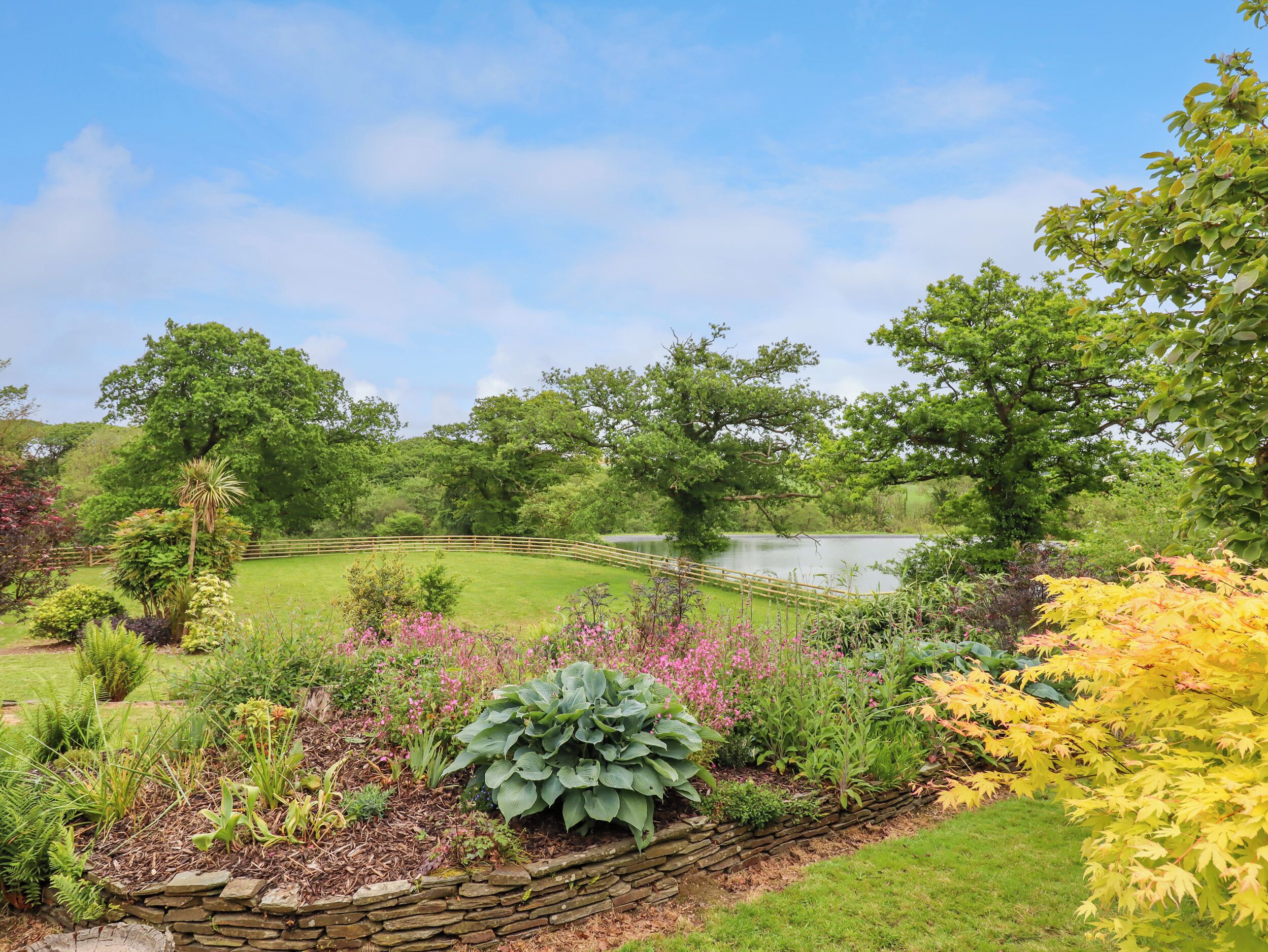 A garden with a pond, stone wall, and various plants.