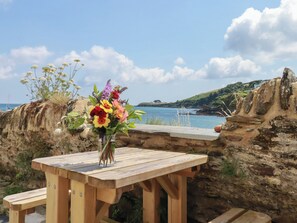 A wooden table with a vase of flowers and a bench, overlooking a coastal landscape with cliffs and the sea. - Chy Rani (St Austell)