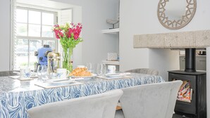 Comedor con una mesa para dos, un jarrón de flores y un estufa de leña negra.