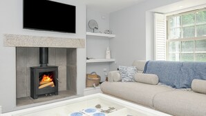 Una sala de estar moderna con chimenea, un televisor de pantalla plana montado sobre ella, un sofá con cojines estampados y una mesa de centro de vidrio con objetos decorativos.