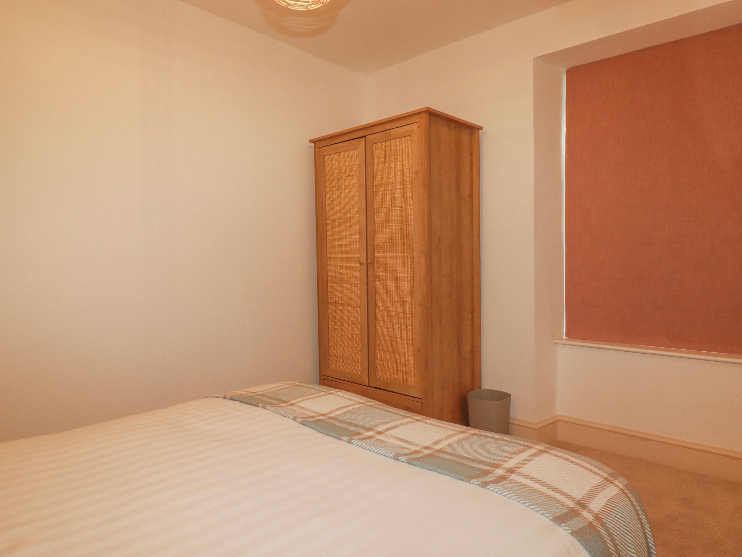 A bedroom with a bed, a wardrobe, and a window with blinds.