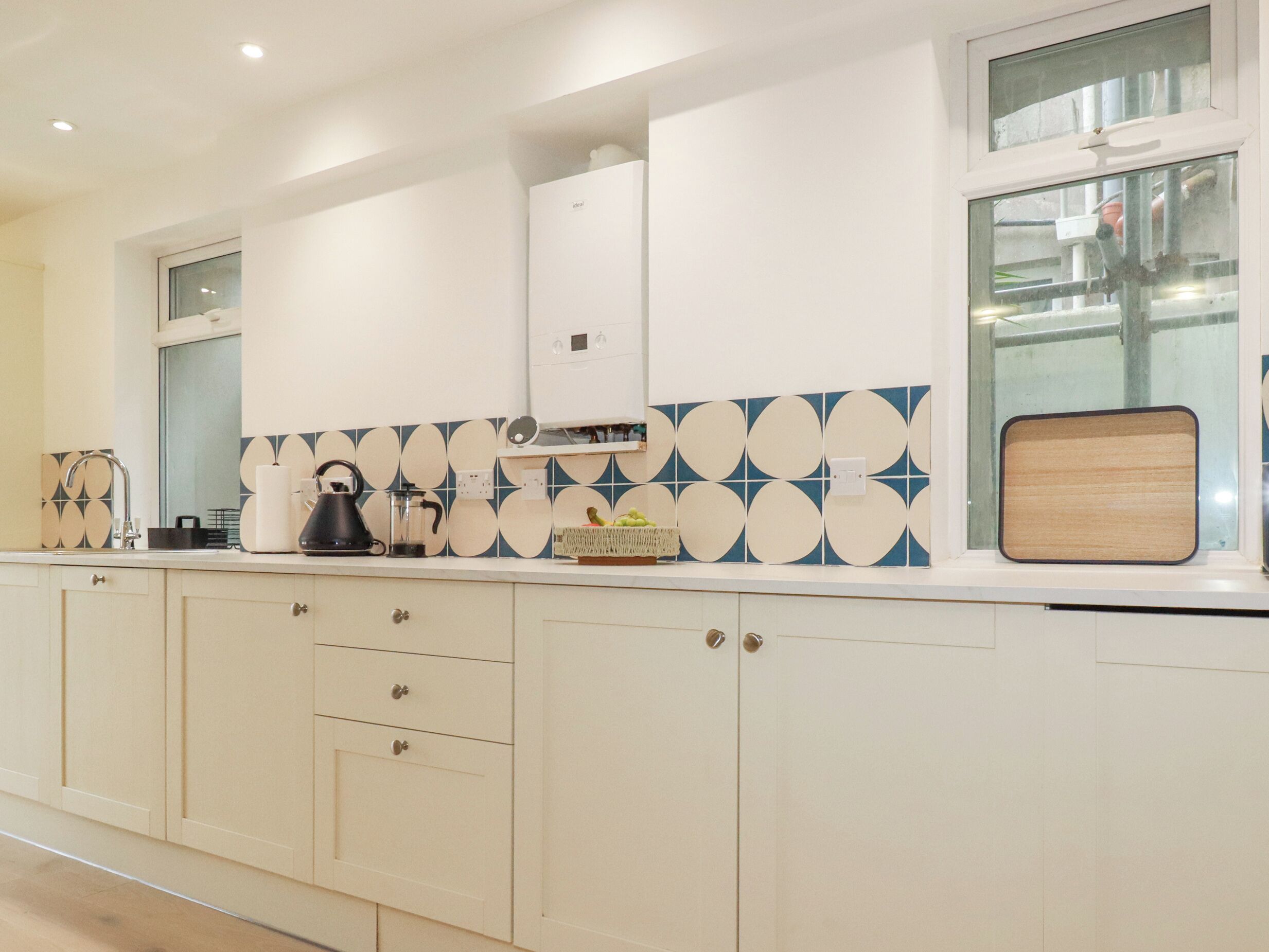 Una cocina moderna con armarios blancos, un salpicadero de azulejos azules y blancos, y un ventanal con vistas al exterior.