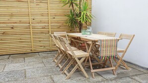 A wooden table and chairs set up on a tiled patio with a wooden fence in the background. - Serendib Cottage (Newquay)