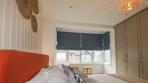 A bedroom with a large bed, a window with a view, a wardrobe, and a hanging light fixture. - Serendib Cottage (Newquay)