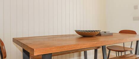A wooden dining table with a woven bowl, surrounded by wooden chairs.