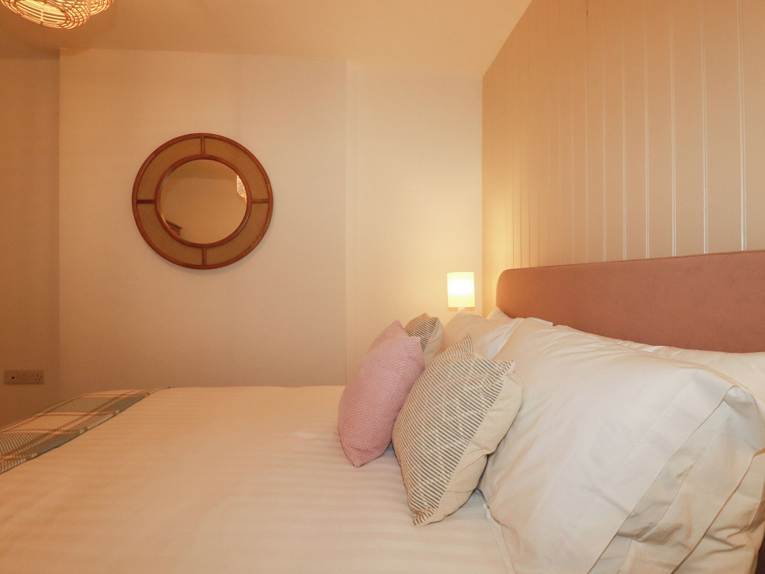 A neatly made bed with pillows, a wall clock, and a bedside lamp.