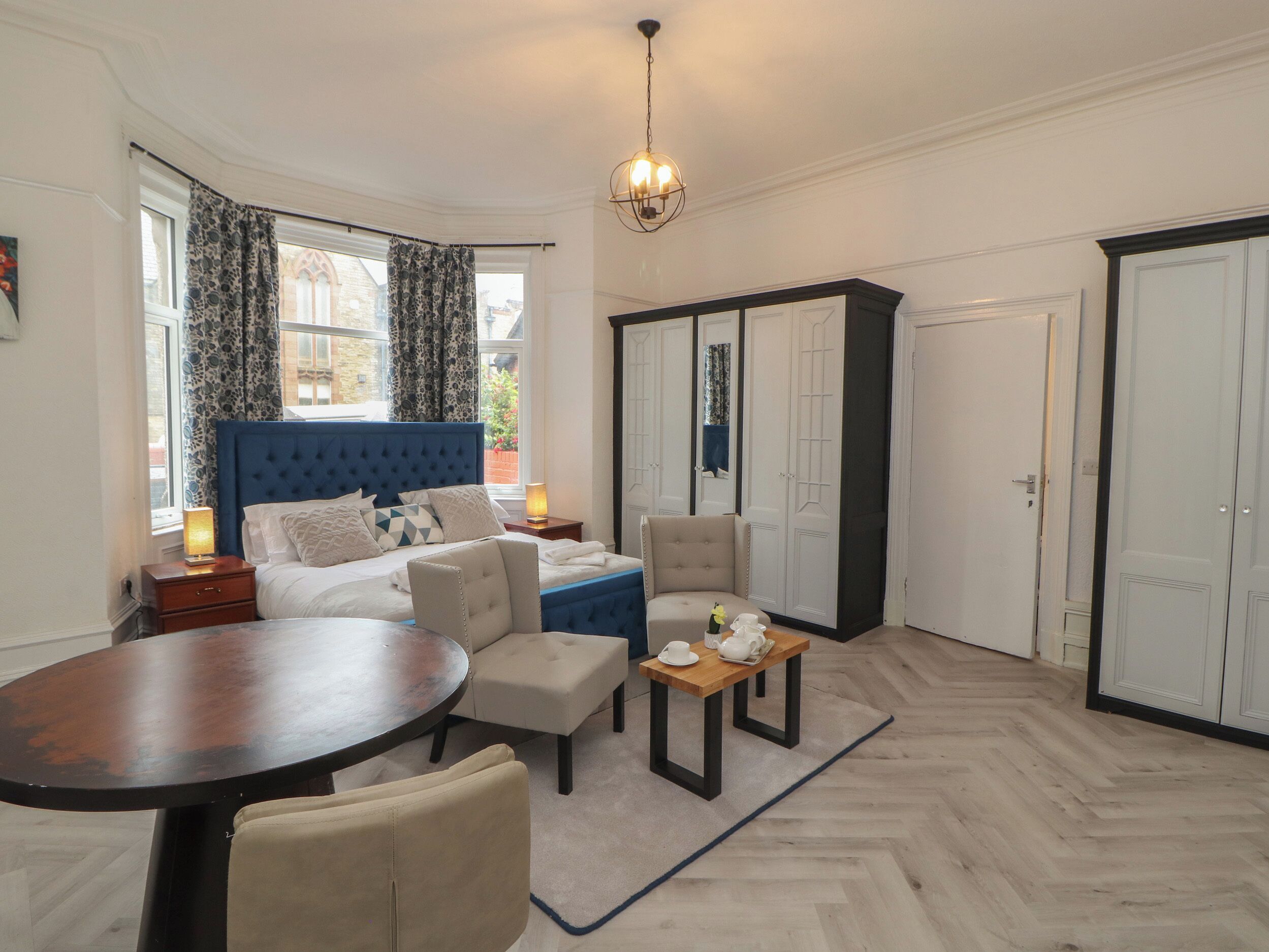 Een slaapkamer met een groot bed, een zithoek met een tafel en stoelen, een kledingkast en een raam met gordijnen.