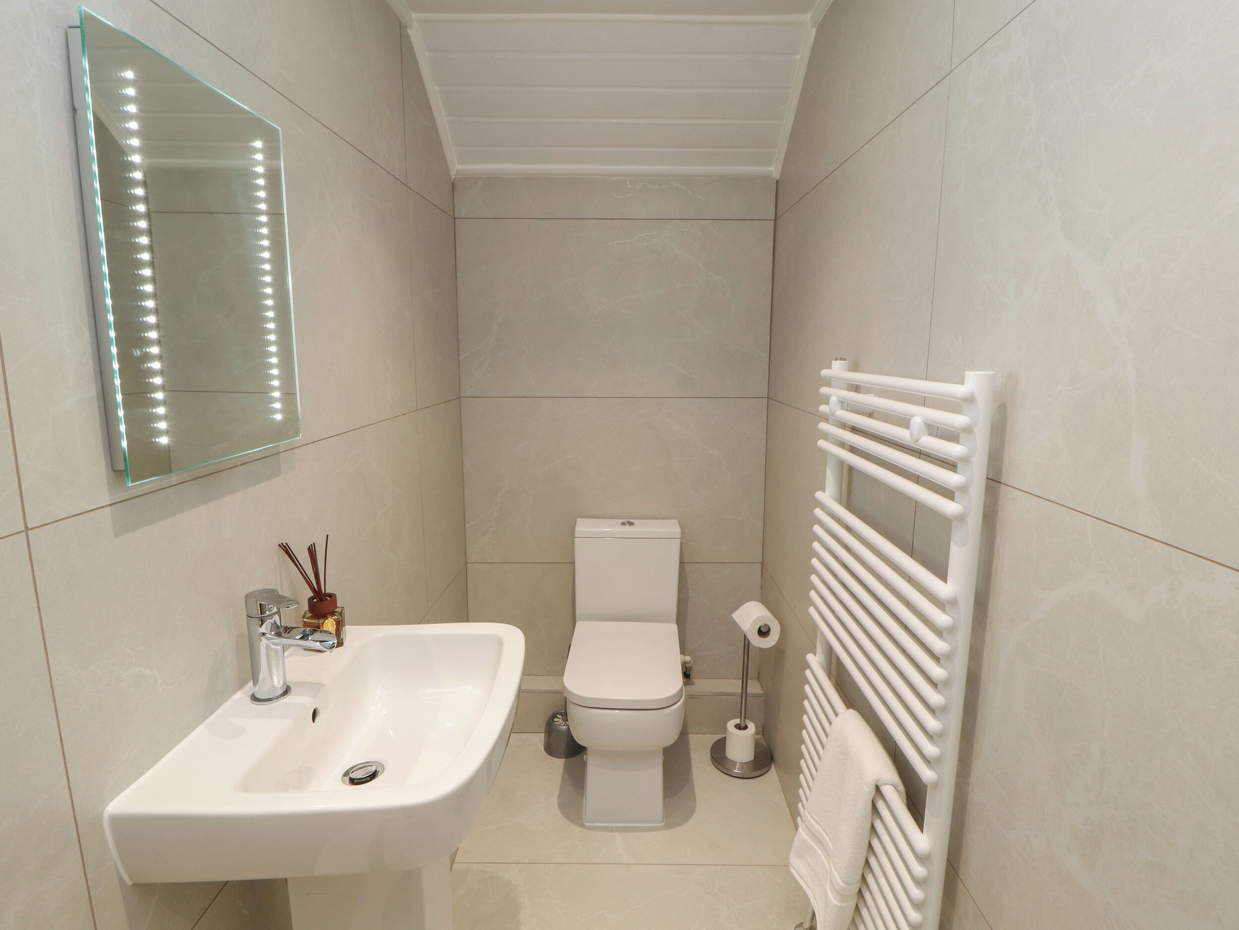 Casa de banho com lavatório branco, sanita e suporte para toalhas.